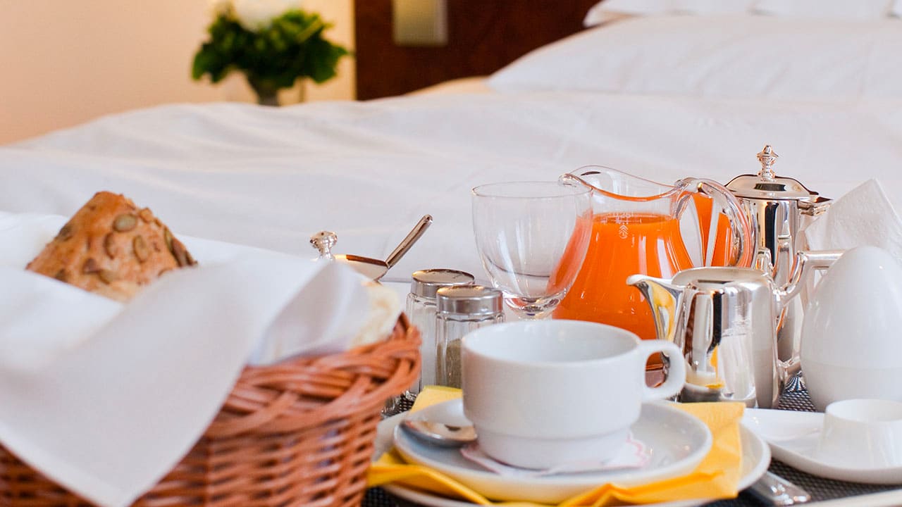 image-breakfast Breakfast on a tray in the hotel room: rolls in a basket, coffee, orange juice, boiled egg, and dishes served on a bed.