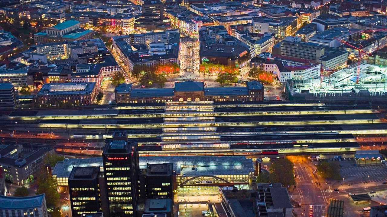 image-hannover-at-night Aerial view of Hanover Central Station at night, brightly lit platforms and the surrounding city center with lights and people.