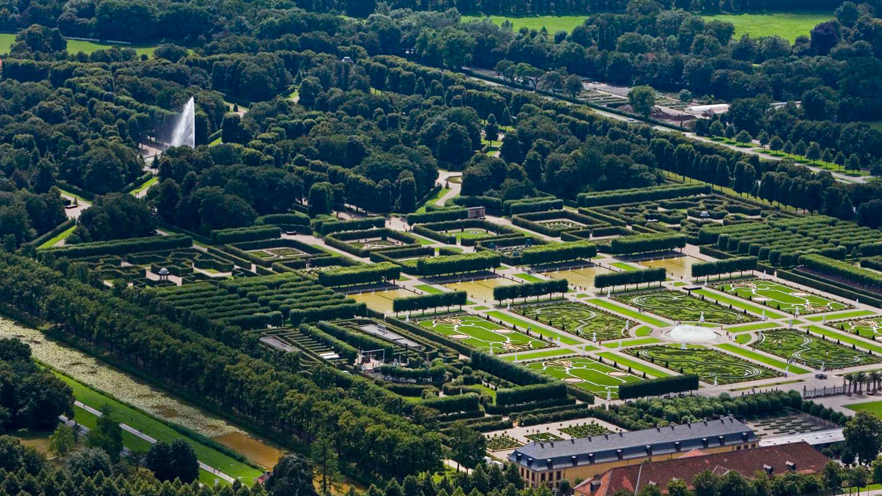 image-hannover-garden Aerial view of the Great Garden in Herrenhausen with geometrically arranged flowerbeds, avenues, and fountains, surrounded by dense rows of trees.