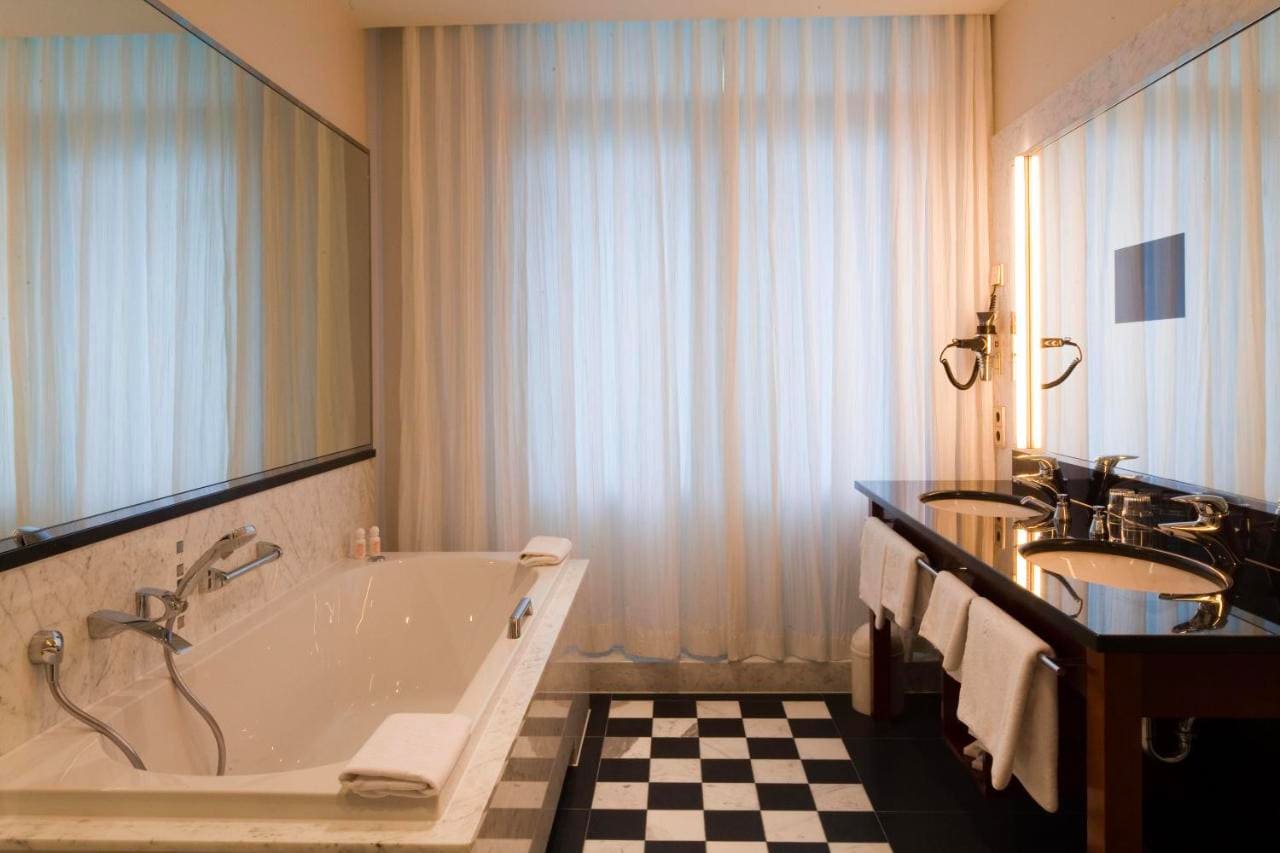 image-room-detail2 Elegant bathroom with a large bathtub, double sink, and black-and-white tiled floor.