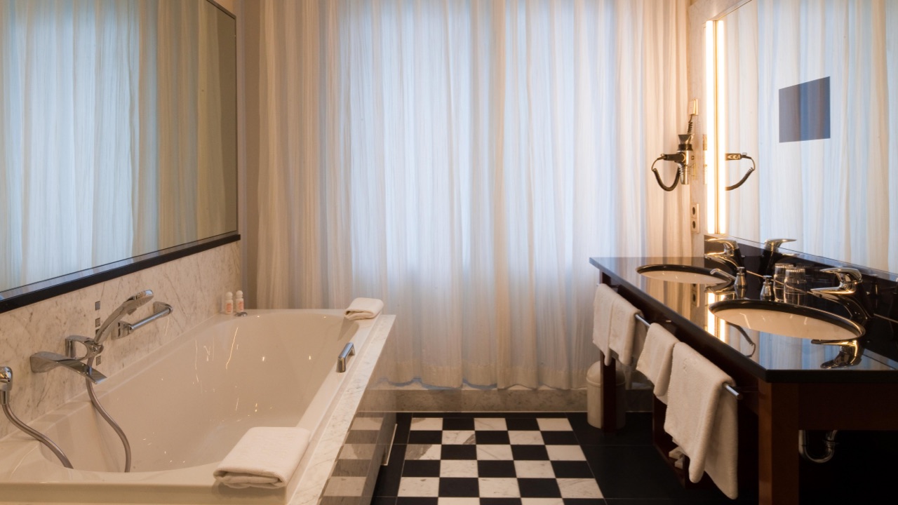Grand-Hotel-Mussmann-Zimmer-Grand-Suite-01 Elegantes Badezimmer mit großer Badewanne, Doppelwaschbecken und schwarz-weißem Fliesenboden.